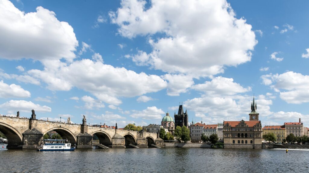 Capture of the historic Charles Bridge and Prague skyline under a bright blue sky.