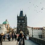 Tourists walking on Charles Bridge in Prague with iconic Old Town Bridge Tower.
